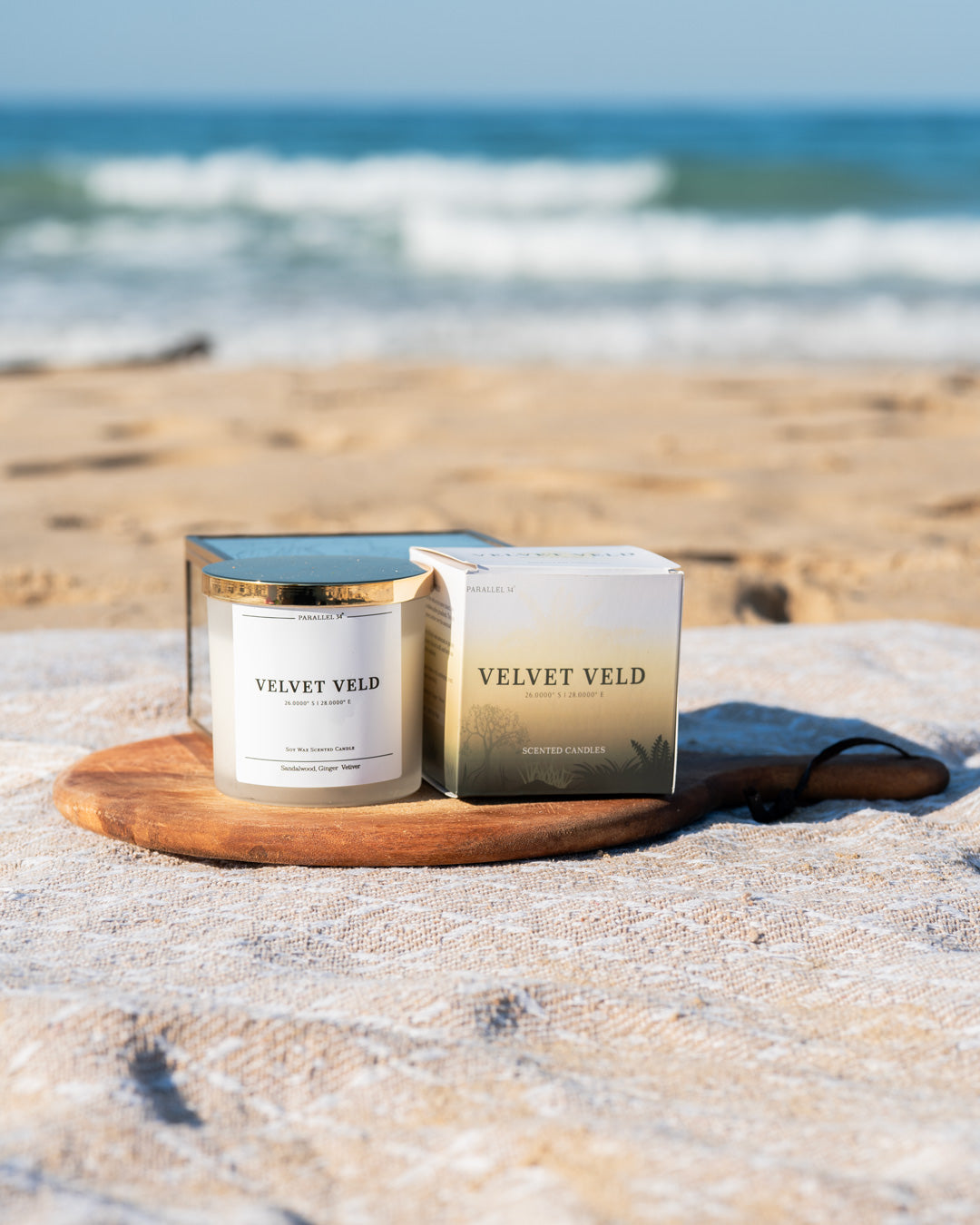 Velvet Yield Luxury candle and packaging on a beach with ocean in the background