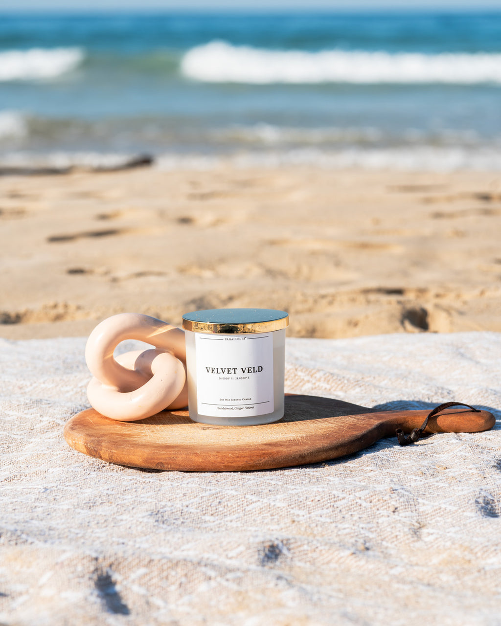 Candle labeled 'Velvet Veld' on a wooden coaster with ocean waves in the background