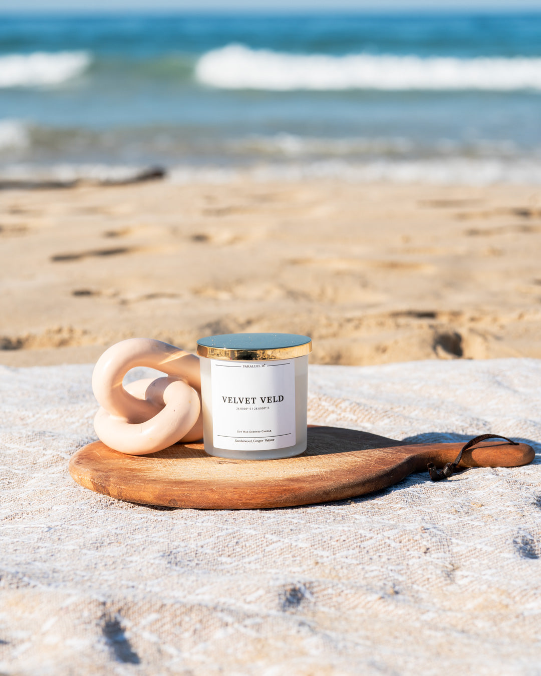 Candle labeled 'Velvet Veld' on a wooden coaster with ocean waves in the background
