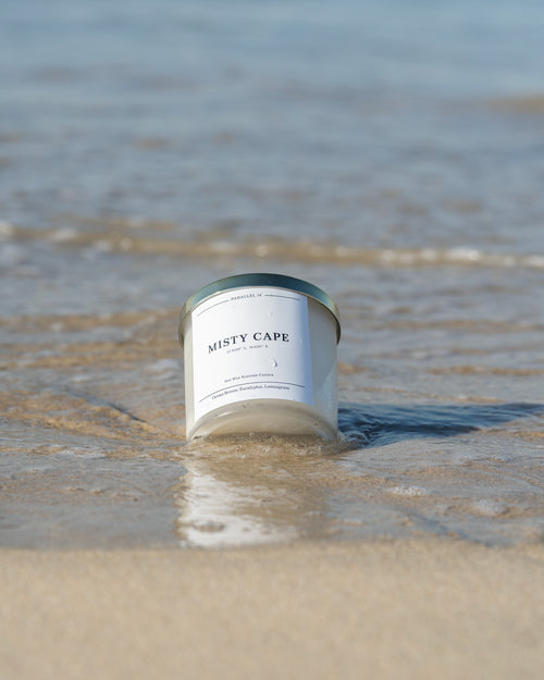 Candle labeled 'Misty Cape' on a beach with water in the background